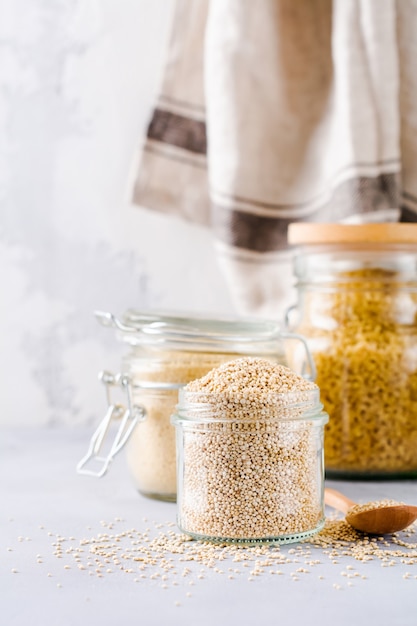 Raw quinoa grains in jar. Healthy vegetarian food on gray kitchen table.  