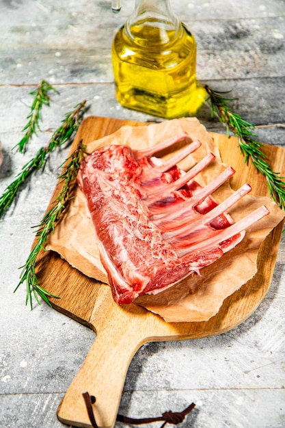 Raw rack of lamb on a cutting board with oil and rosemary