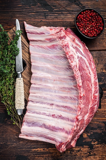 Raw rack of lamb ribs on butcher cutting board with herbs