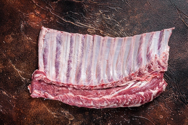 Raw rack of lamb ribs on butcher table. Dark background. Top view.