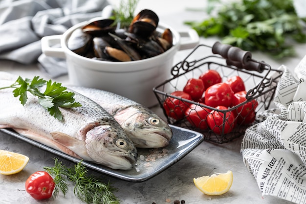 raw rainbow trout fish on a plate, greens and fresh vegetables for preparing healthy and tasty food. Healthy diet and delicious culinary concept.