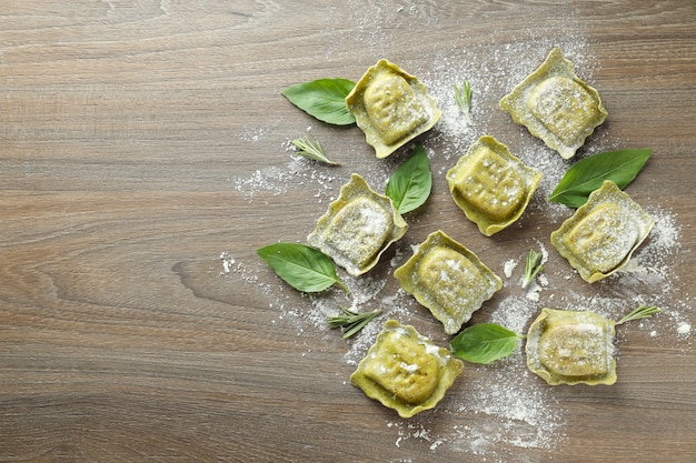 Raw ravioli with flour and basil on wooden background