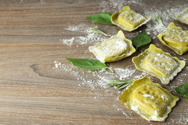 Raw ravioli with flour and basil on wooden background