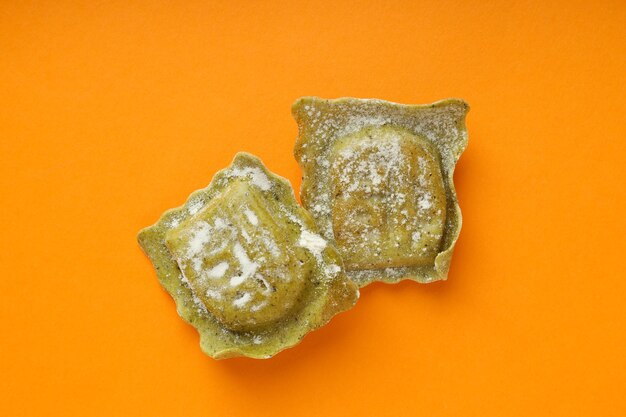 Raw ravioli with flour on orange background