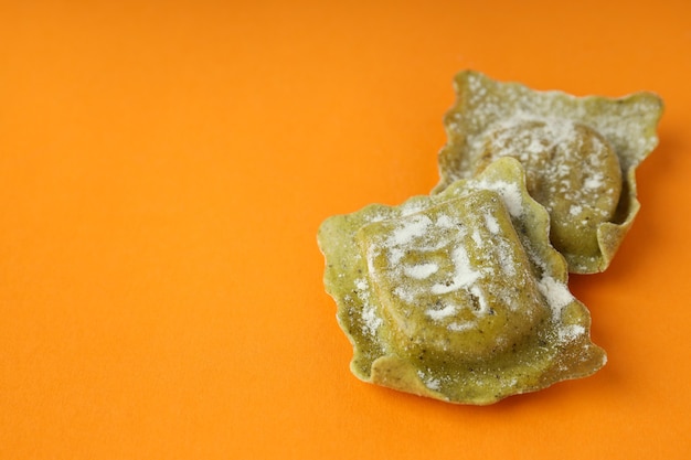 Raw ravioli with flour on orange background