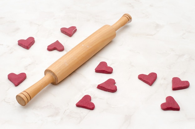 Raw red heart-shaped cookies on a white table with a rolling pin, baking for Valentine's Day