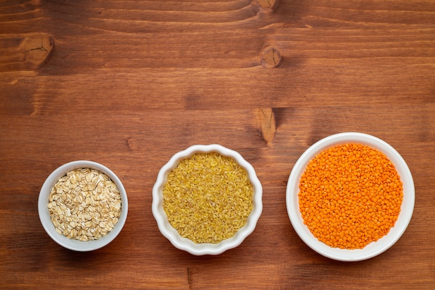 Raw red lentils, , bulgur, oak flakes in white bowls