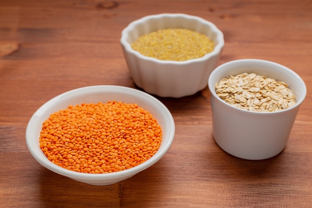 Raw red lentils, , bulgur, oak flakes in white bowls.