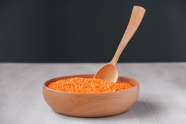 Raw red lentils in a wooden bowl and spoon on a white table