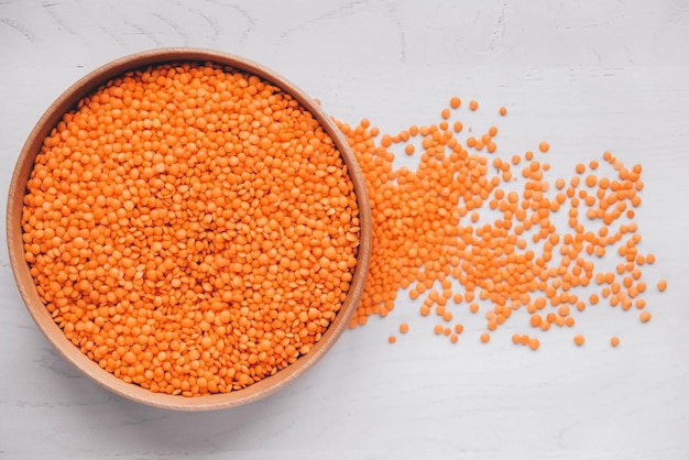 Raw red lentils in a wooden bowl on a white table