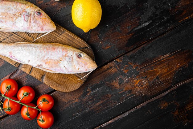 Raw red mullet or sultanka fresh whole fish set, with ingredients and herbs, on old dark  wooden table background, top view flat lay, with copy space for text