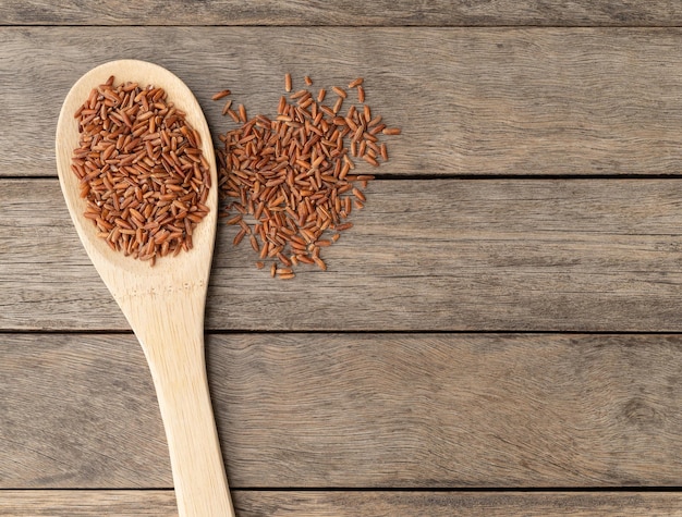 Raw red rice in a spoon over wooden table with copy space