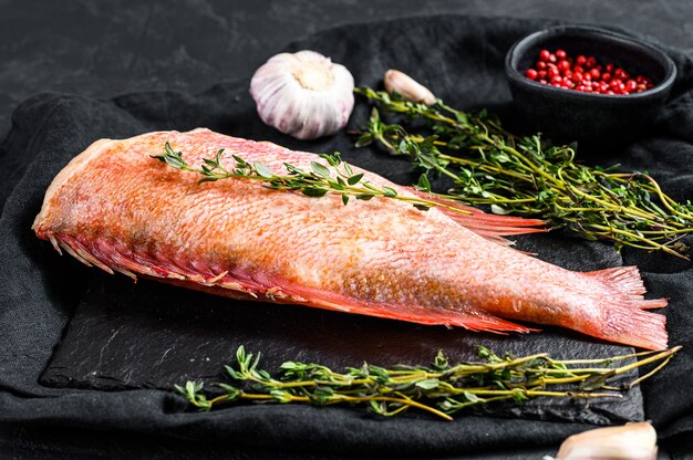 Raw red sea perch on a stone Board with thyme. Top view