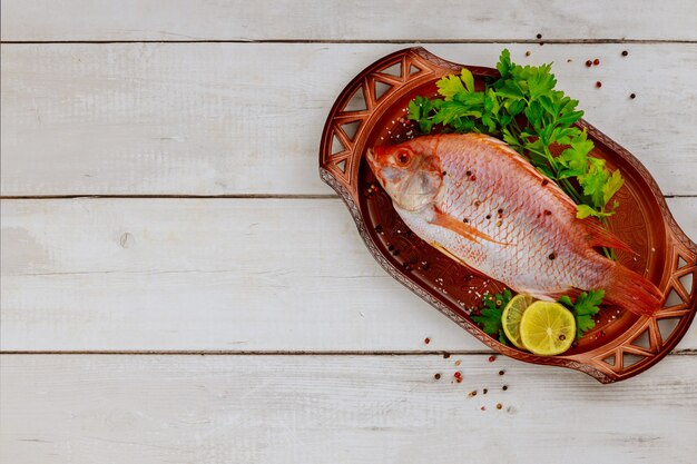 Pesce rosso crudo di tilapia con erbe e limone e calce su fondo di legno bianco. vista dall'alto, copia dello spazio.