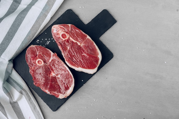 Raw rib-eye beef steak on wooden cutting board on gray