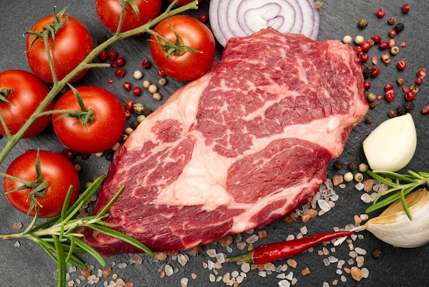 Raw rib eye steak with spices and vegetables