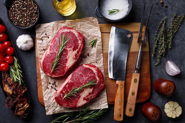 Raw ribeye beef steak with herbs on cutting board Raw meat sirloin over dark stone background