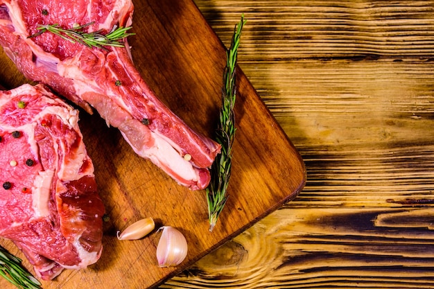 Raw ribeye steak, spices, rosemary and garlic on wooden cutting board. Top view