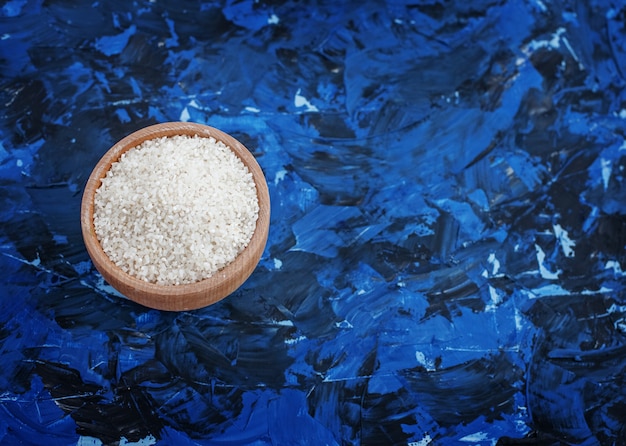 Raw rice in a bowl on a blue background. Ingredient. 