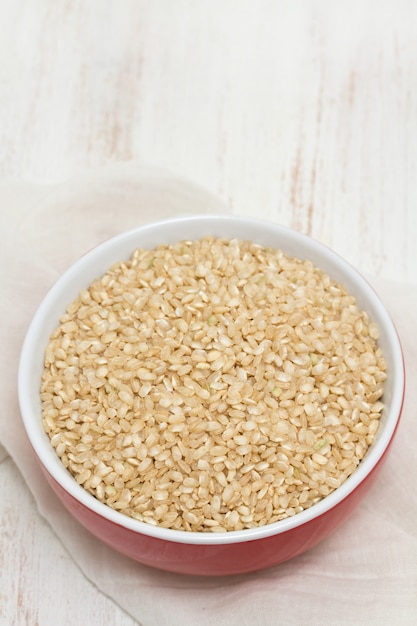 Raw rice in red bowl on wooden surface