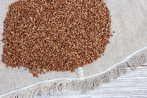 Raw roasted buckwheats scattered on light wood and coarse cloth