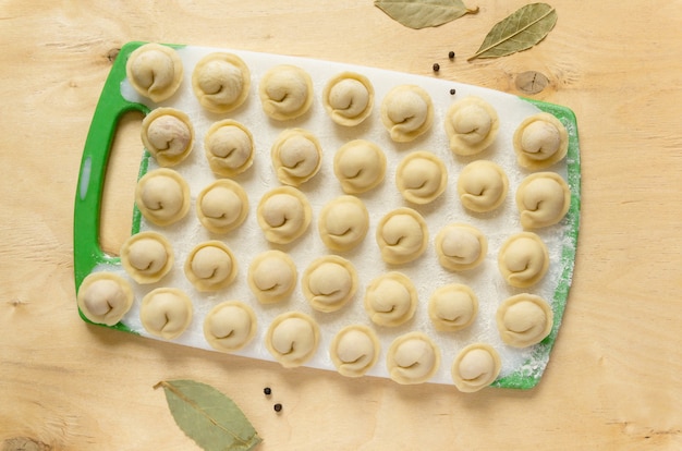 Raw russian dumplings with bay leaf and pepper on wooden table