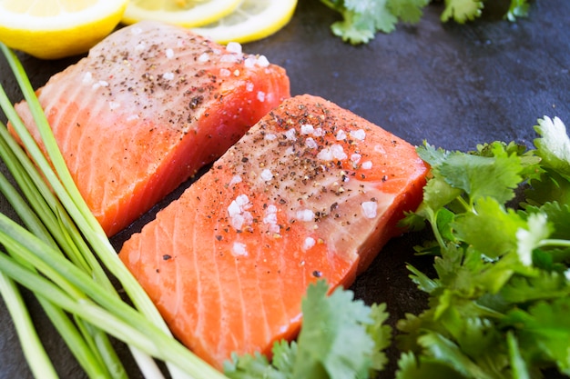 Foto filetto di salmone crudo e ingredienti per cucinare su uno sfondo scuro in stile rustico. vista dall'alto