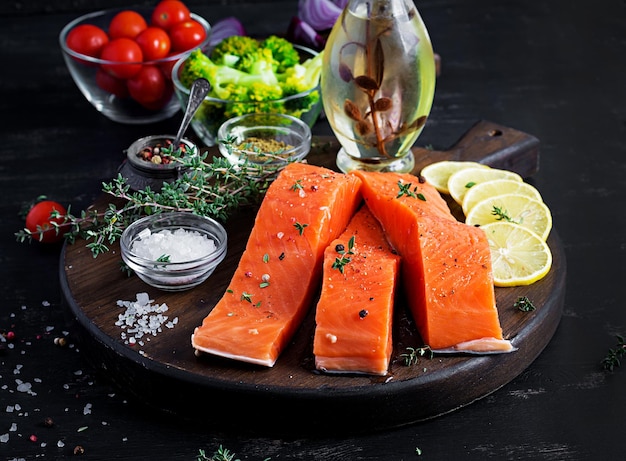 Raw salmon fillet and ingredients for cooking on a dark background in a rustic style