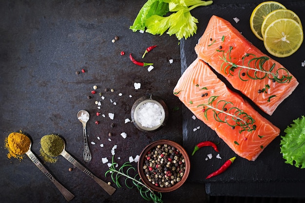 Raw salmon fillet and ingredients for cooking on a dark background in a rustic style