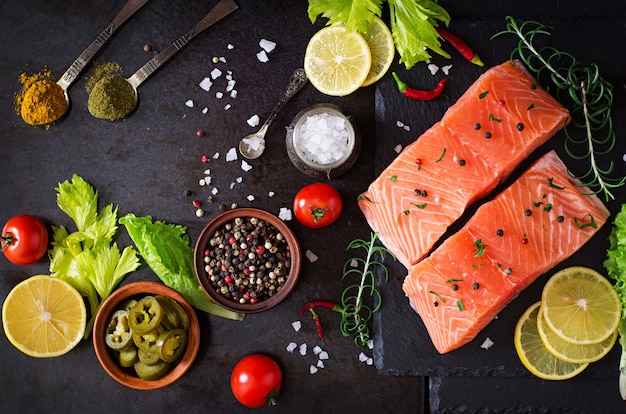 Filetto di salmone crudo e ingredienti per cucinare su una superficie scura in stile rustico.