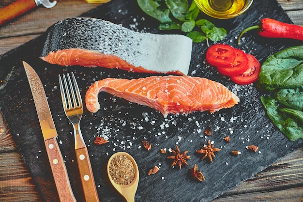 Photo raw salmon fillet and ingredients for cooking on a dark table