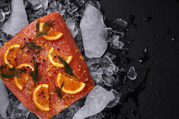 Raw salmon fillet with orange slices on pieces of ice on a black background