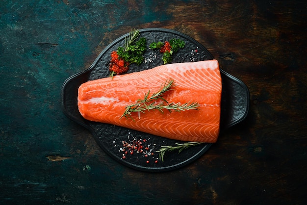 Raw salmon fillet with rosemary on a black stone plate. On a dark background. Flat lay.