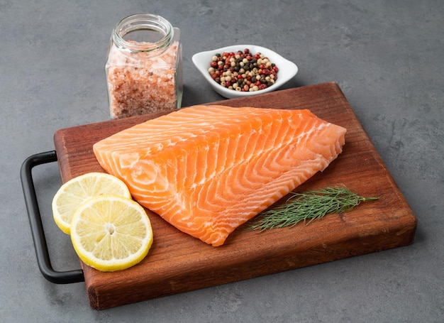 Raw salmon fillet with seasonings over wooden board