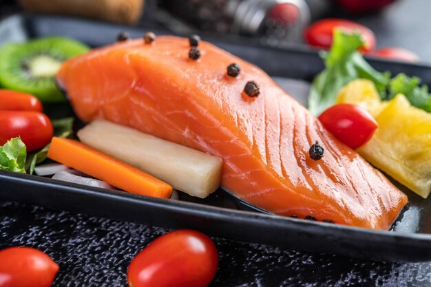 Raw salmon fillets pepper kiwi pineapples and rosemary onto a plate and black cement floor