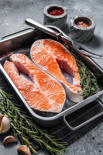 Raw Salmon Fish Steaks  prepared for cooking with thyme and rosemary. Gray background. Top view.