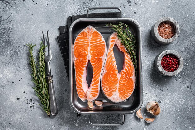 Raw Salmon Fish Steaks  prepared for cooking with thyme and rosemary. Gray background. Top view.