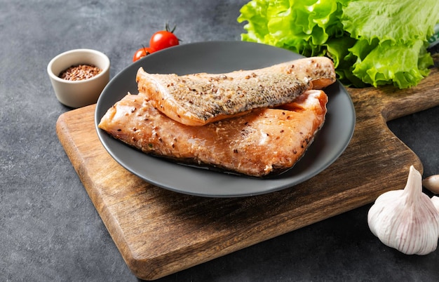 Raw salmon greased with marinade with spices on a plate on a dark background with fresh herbs and vegetables