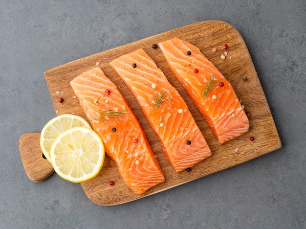 Raw salmon slices with seasonings over wooden board