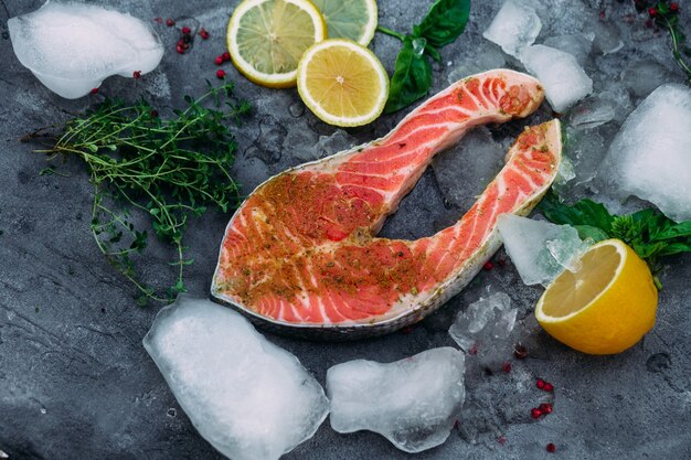 Raw salmon steak with herbs ice and lemon on gray background