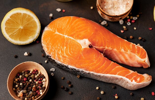 Raw salmon steaks with spices, herbs, salt and lemon on a stone background.