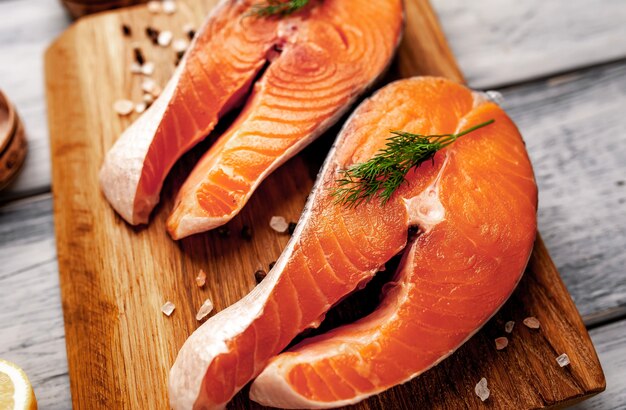 Raw salmon steaks with spices, herbs, salt and lemon on a wood background.