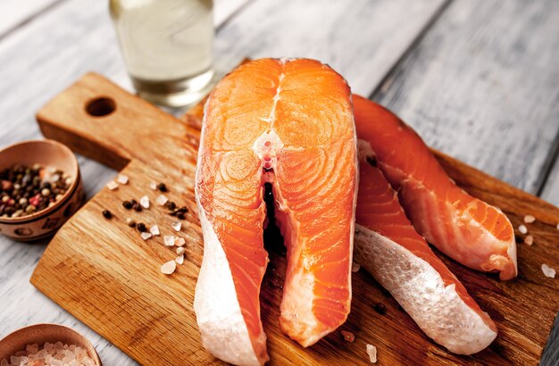 Raw salmon steaks with spices, herbs, salt and lemon on a wood background.