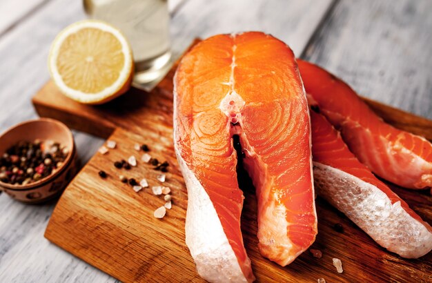 Raw salmon steaks with spices, herbs, salt and lemon on a wood background.