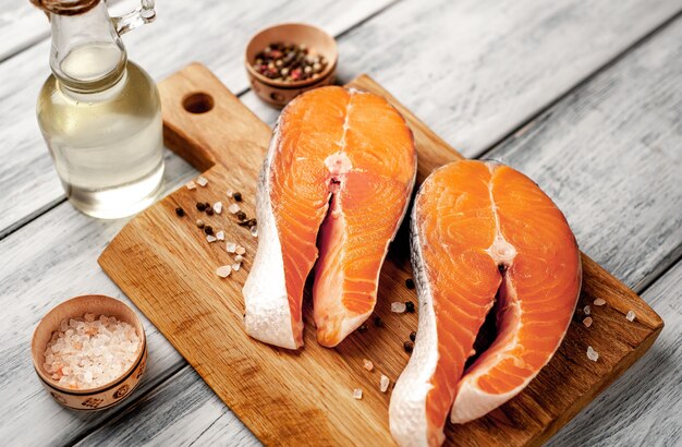 Raw salmon steaks with spices, herbs, salt and lemon on a wood background.