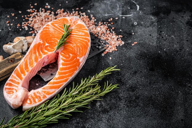 Raw Salmon trout Fish Steak on butcher table with meat cleaver Black background Top view Copy space