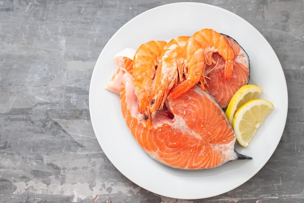 Raw salmon with lemon on white dish on ceramic table