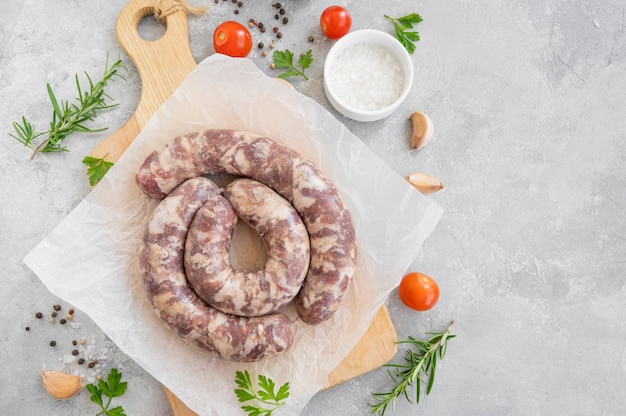 Raw sausages on a board with spices and fresh herbs on a gray concrete background. copy space.