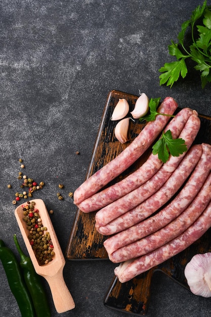 Salsicce crude bratwurst o salsicce con ingredienti sul tagliere con spezie su uno sfondo di pietra con spazio per la copia sfondo di cottura degli alimenti vista dall'alto