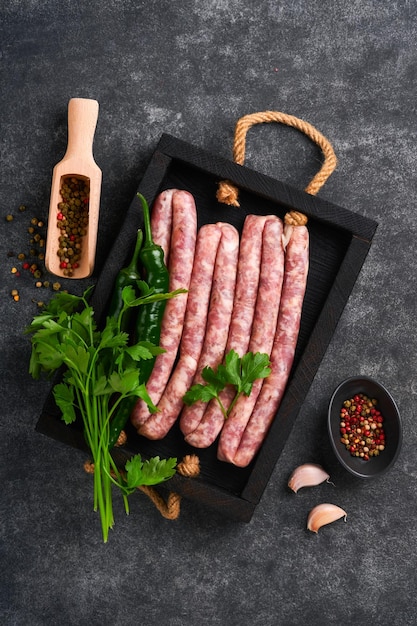 Raw sausages bratwurst or sausages with ingredients on cutting\
board with spices on a stone background with copy space food\
cooking background top view